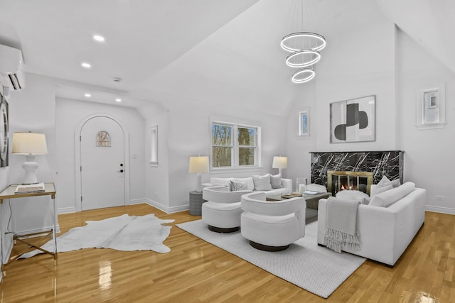 living area with a wall unit AC, a premium fireplace, wood finished floors, and lofted ceiling