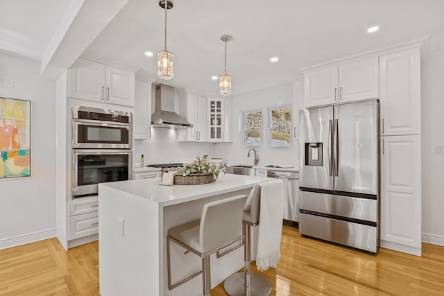 kitchen featuring wall chimney exhaust hood, glass insert cabinets, appliances with stainless steel finishes, light wood-type flooring, and white cabinetry