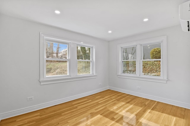 unfurnished room with light wood-style floors, a wall mounted air conditioner, baseboards, and recessed lighting