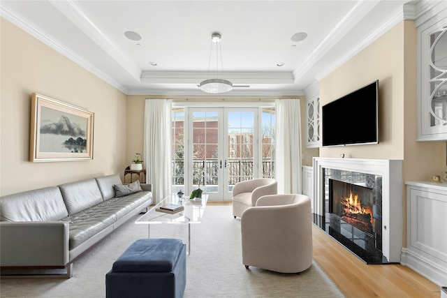 living room with a premium fireplace, a tray ceiling, light hardwood / wood-style flooring, and french doors