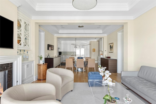 living room featuring sink, light hardwood / wood-style flooring, an inviting chandelier, a tray ceiling, and ornamental molding