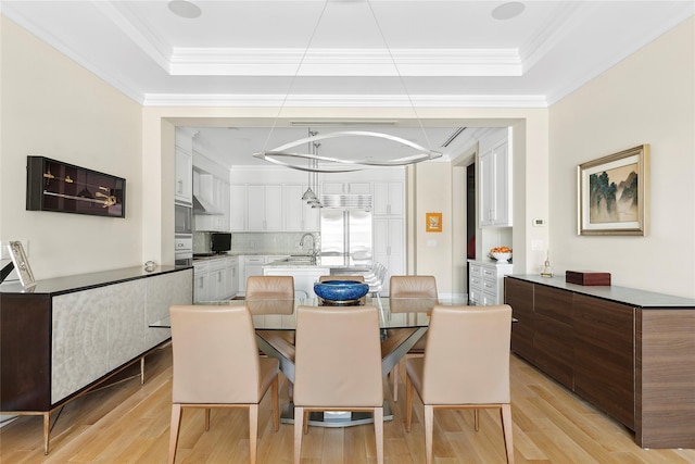 dining room featuring crown molding, sink, a tray ceiling, and light hardwood / wood-style flooring