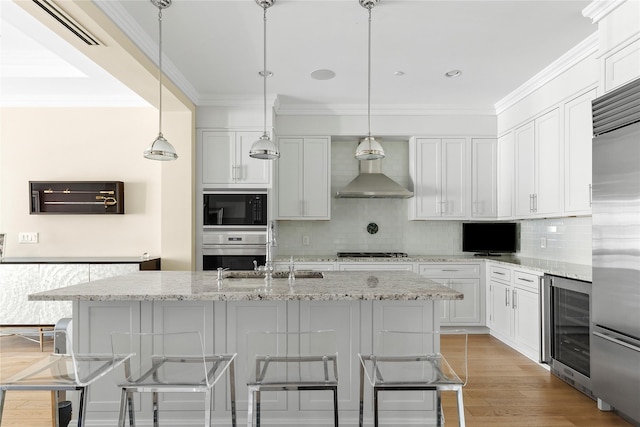 kitchen featuring beverage cooler, decorative light fixtures, a kitchen island with sink, and black appliances