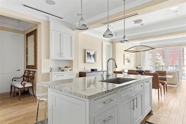 kitchen featuring white cabinetry, sink, a center island with sink, and pendant lighting