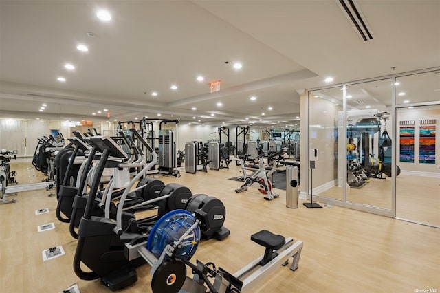 workout area featuring a raised ceiling and light wood-type flooring