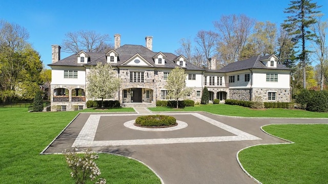 rear view of house with a lawn, stone siding, and driveway