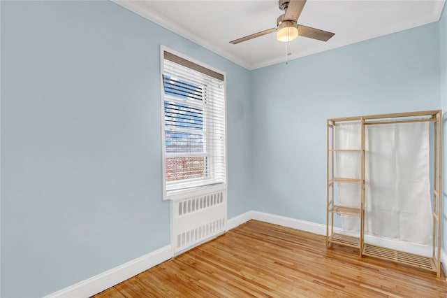 empty room featuring radiator heating unit, a ceiling fan, ornamental molding, light wood-type flooring, and baseboards