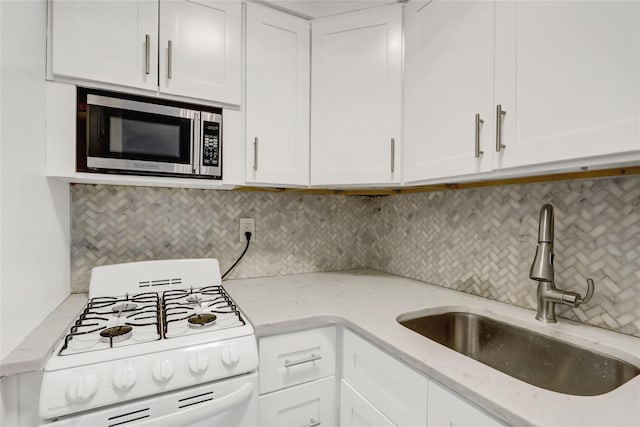 kitchen with white range with gas stovetop, stainless steel microwave, a sink, and white cabinets