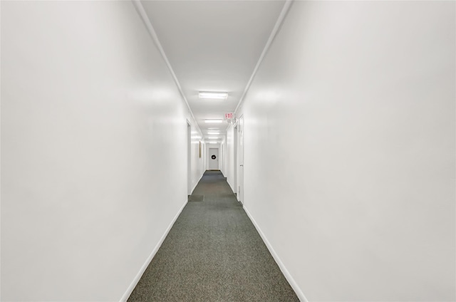 corridor with baseboards and dark carpet