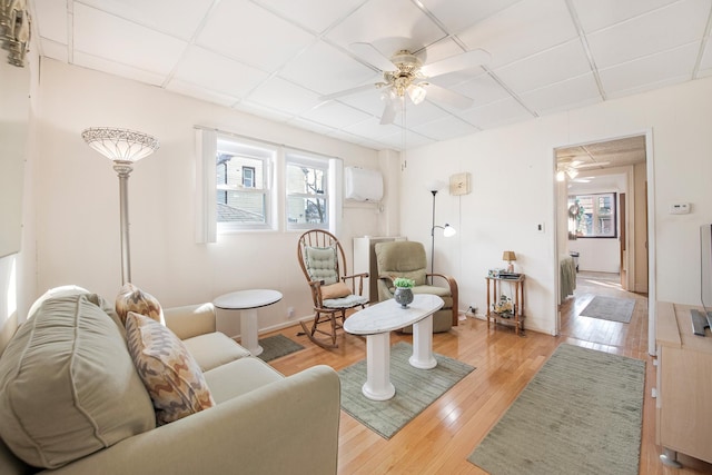 living room featuring ceiling fan, a wall mounted air conditioner, light hardwood / wood-style floors, and a drop ceiling