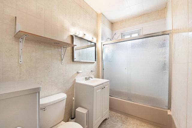 full bathroom with enclosed tub / shower combo, vanity, toilet, and tile walls