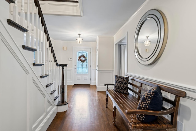 foyer entrance with dark wood-style floors, a wainscoted wall, stairs, crown molding, and a decorative wall