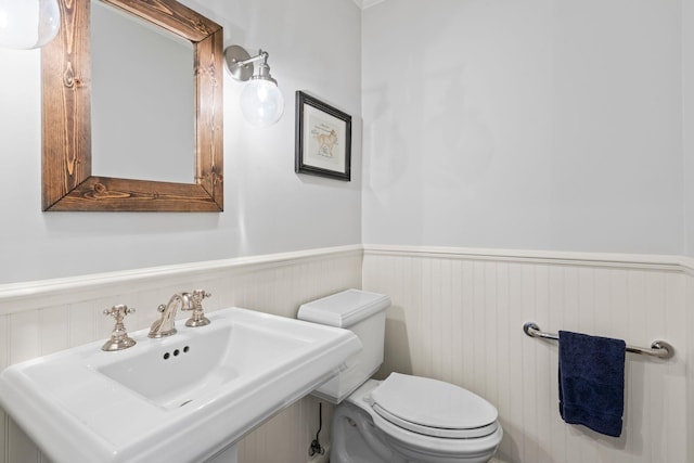 half bath with toilet, a sink, and wainscoting