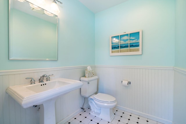 bathroom with toilet, tile patterned floors, a sink, and wainscoting