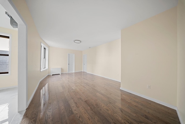 unfurnished room featuring radiator heating unit, baseboards, and wood finished floors