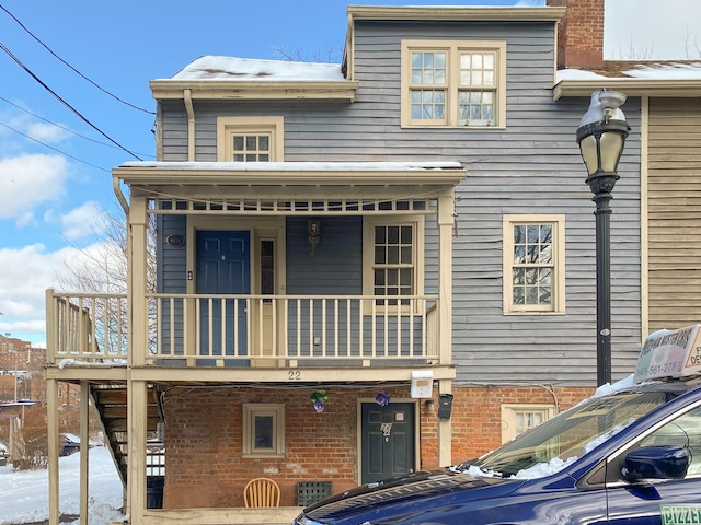 snow covered property with a balcony and a porch