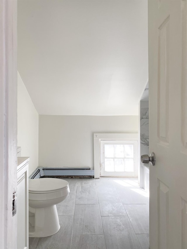 bathroom featuring baseboard heating, lofted ceiling, vanity, and toilet