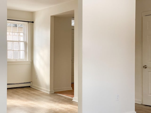 corridor with a baseboard heating unit and light hardwood / wood-style floors