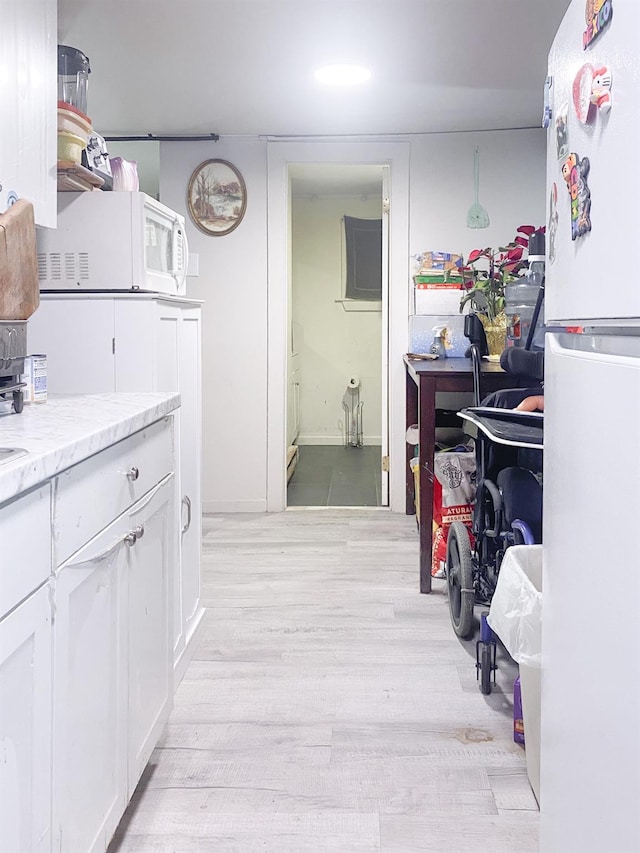 kitchen with white cabinetry, white appliances, and light hardwood / wood-style flooring