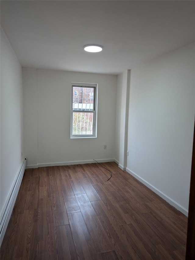 spare room featuring baseboard heating and dark hardwood / wood-style floors