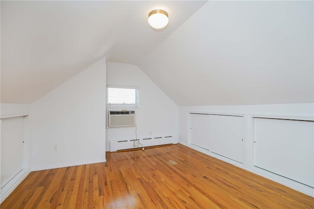 additional living space with lofted ceiling, a baseboard heating unit, cooling unit, and hardwood / wood-style floors