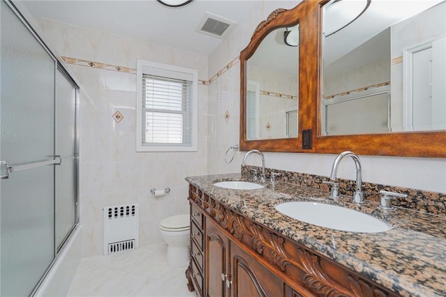 full bathroom featuring toilet, combined bath / shower with glass door, tile walls, radiator heating unit, and vanity