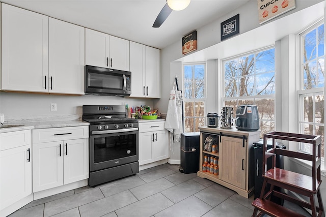 kitchen featuring white cabinetry, light stone counters, light tile patterned floors, appliances with stainless steel finishes, and ceiling fan