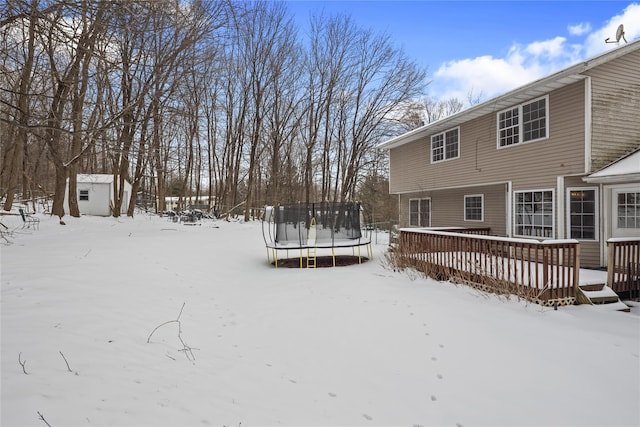 snowy yard with an outbuilding, a storage unit, a trampoline, and a wooden deck