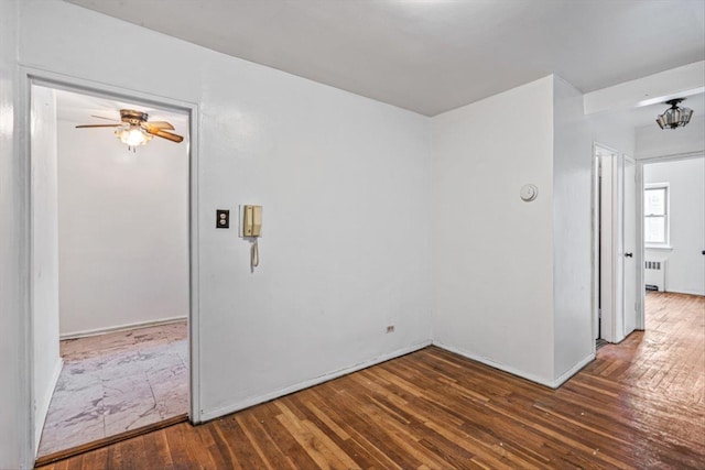 empty room featuring dark wood-type flooring, ceiling fan, and radiator