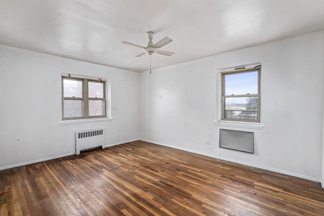 empty room featuring ceiling fan, radiator, a wealth of natural light, and dark hardwood / wood-style floors