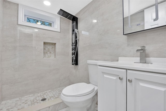 bathroom with tiled shower, vanity, tile walls, and toilet