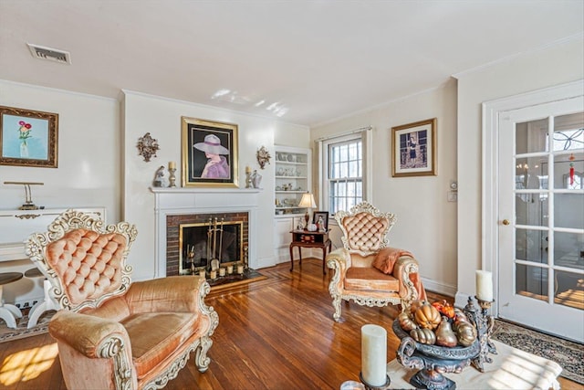 living room featuring built in shelves, a fireplace, visible vents, ornamental molding, and wood finished floors