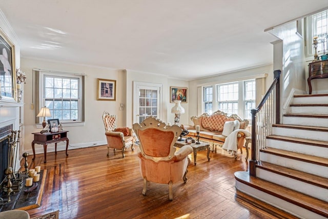 living area with a fireplace with raised hearth, crown molding, stairway, and wood finished floors