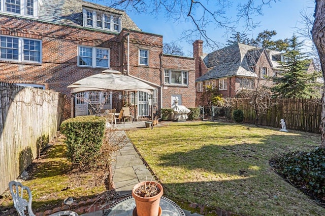 rear view of house featuring brick siding, a fenced backyard, a yard, and a gazebo