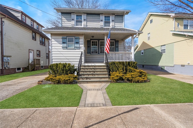 american foursquare style home featuring a porch, a front yard, and a shingled roof