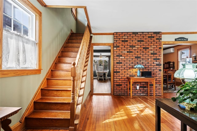 staircase with ornamental molding, wood finished floors, and a wall mounted AC