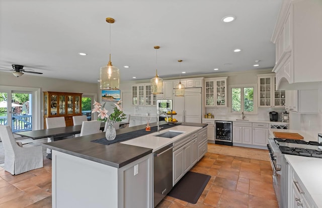 kitchen with built in appliances, hanging light fixtures, beverage cooler, a kitchen island with sink, and white cabinets