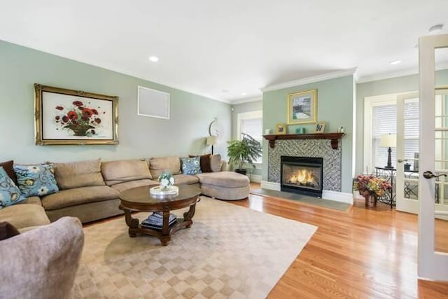 living room featuring a tiled fireplace, wood-type flooring, crown molding, and french doors