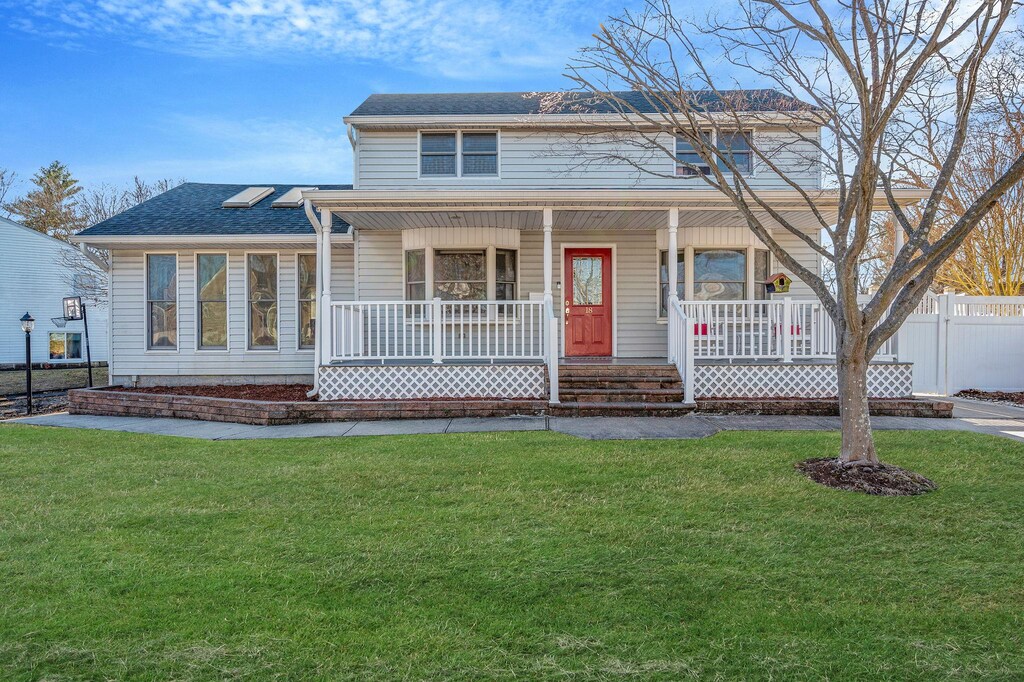 view of front facade featuring roof with shingles, covered porch, a front lawn, and fence