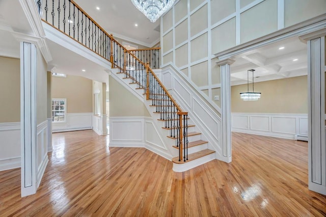 stairway with ornate columns, hardwood / wood-style flooring, and a notable chandelier