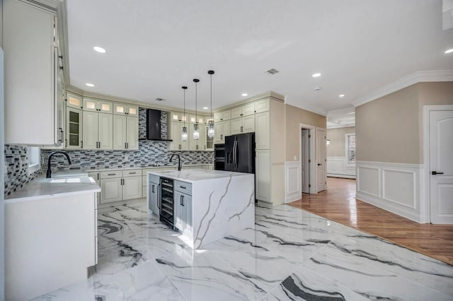 kitchen with sink, a center island with sink, light stone countertops, black fridge with ice dispenser, and decorative light fixtures