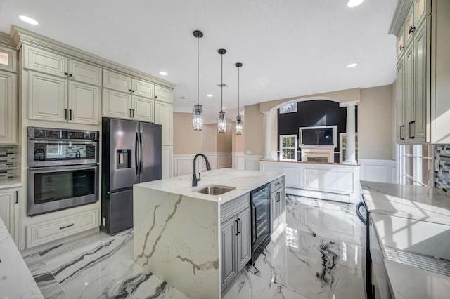 kitchen with pendant lighting, stainless steel appliances, light stone countertops, a center island with sink, and cream cabinetry