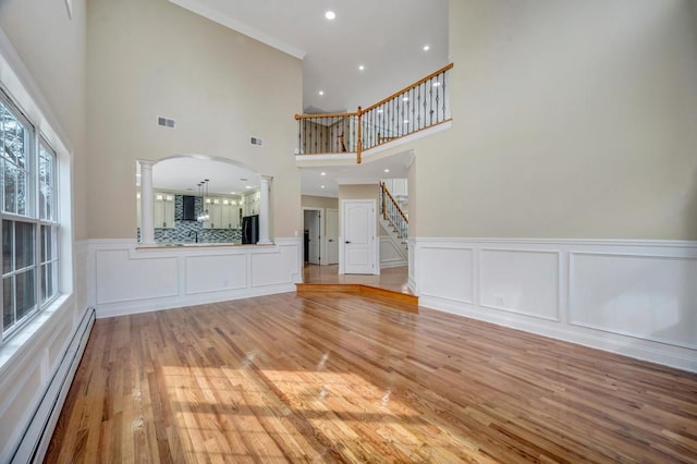 unfurnished living room with ornate columns, a baseboard radiator, and light wood-type flooring