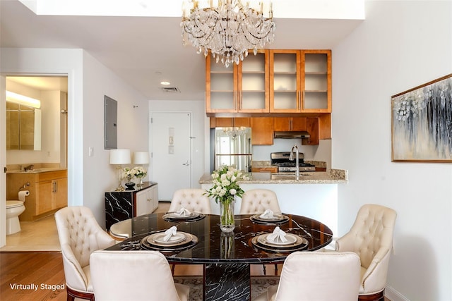 dining area featuring an inviting chandelier, sink, electric panel, and light wood-type flooring