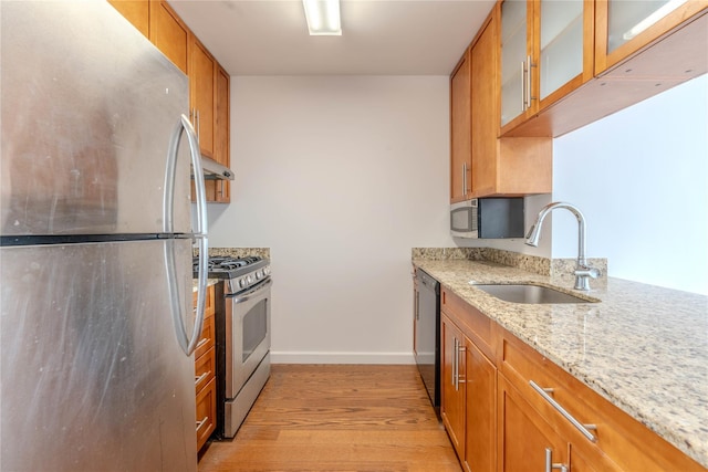 kitchen with sink, stainless steel appliances, light hardwood / wood-style floors, and light stone countertops