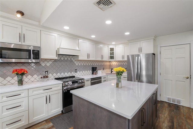 kitchen with premium range hood, visible vents, white cabinetry, appliances with stainless steel finishes, and glass insert cabinets