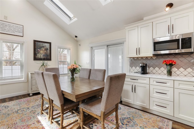 dining area with lofted ceiling with skylight, light wood-style flooring, and baseboards