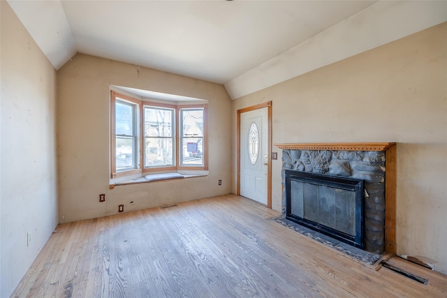 unfurnished living room featuring lofted ceiling, a stone fireplace, and light wood-type flooring