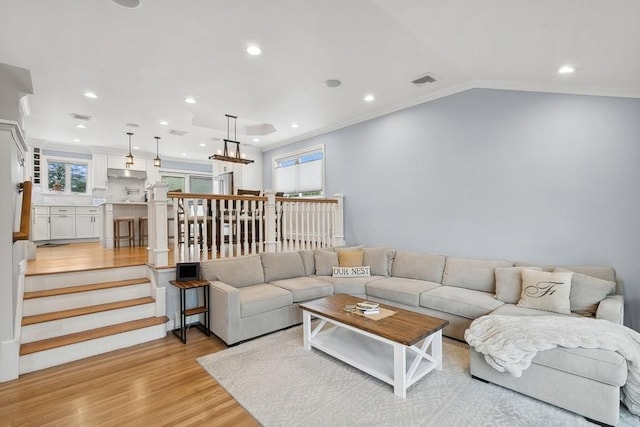 living area with light wood-style floors, lofted ceiling, visible vents, and stairway