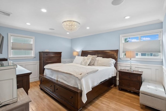 bedroom featuring light wood-style floors, visible vents, a wainscoted wall, and ornamental molding